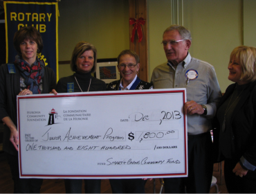 Five adults standing behind a very large cheque made out to Junior Achievement for $1,800