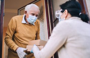 Woman delivering small boxes to an elderly man both wearing ppe