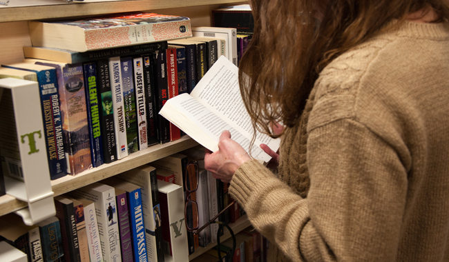 girl looking inside a book in front of a shelf full of books